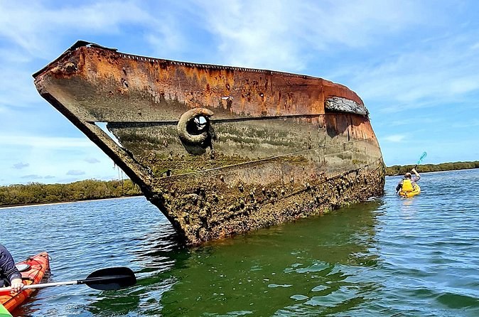 A kayaker paddling past the rusted bow of a wreck