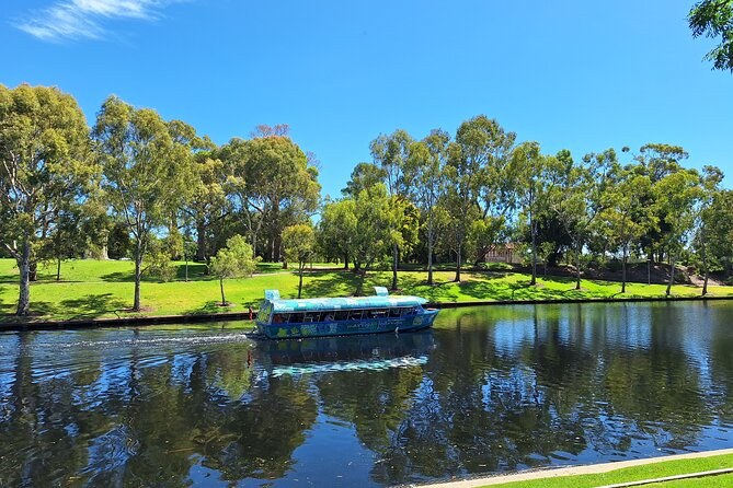 A small river boat on the Torrens below lawns and gum trees